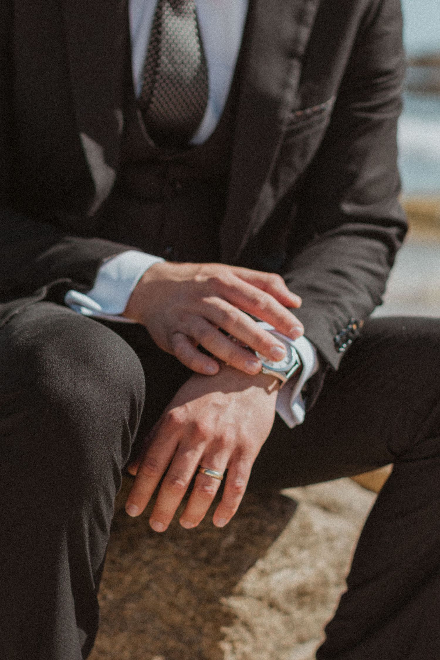 Close-up detail shot of a groom's hands and watch with suit sleeve.