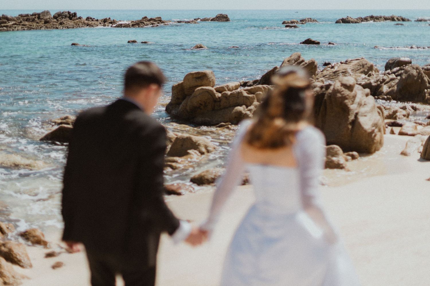Couple walking hand in hand along rocky beach shoreline.