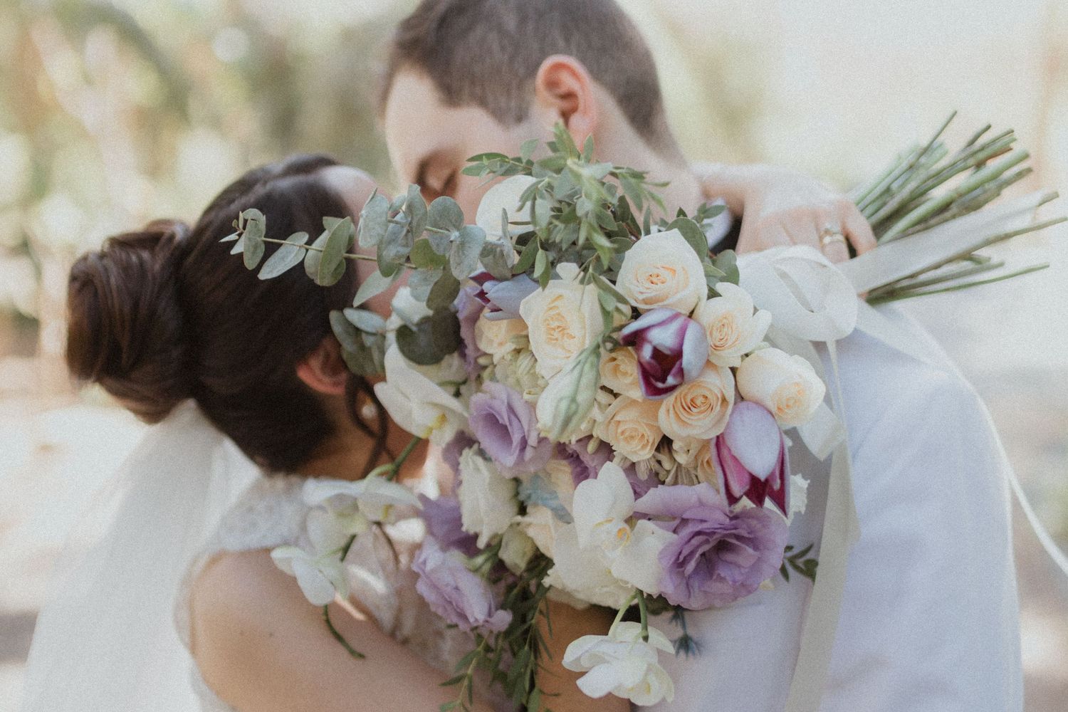 Close up of couple sharing intimate moment behind wedding bouquet.