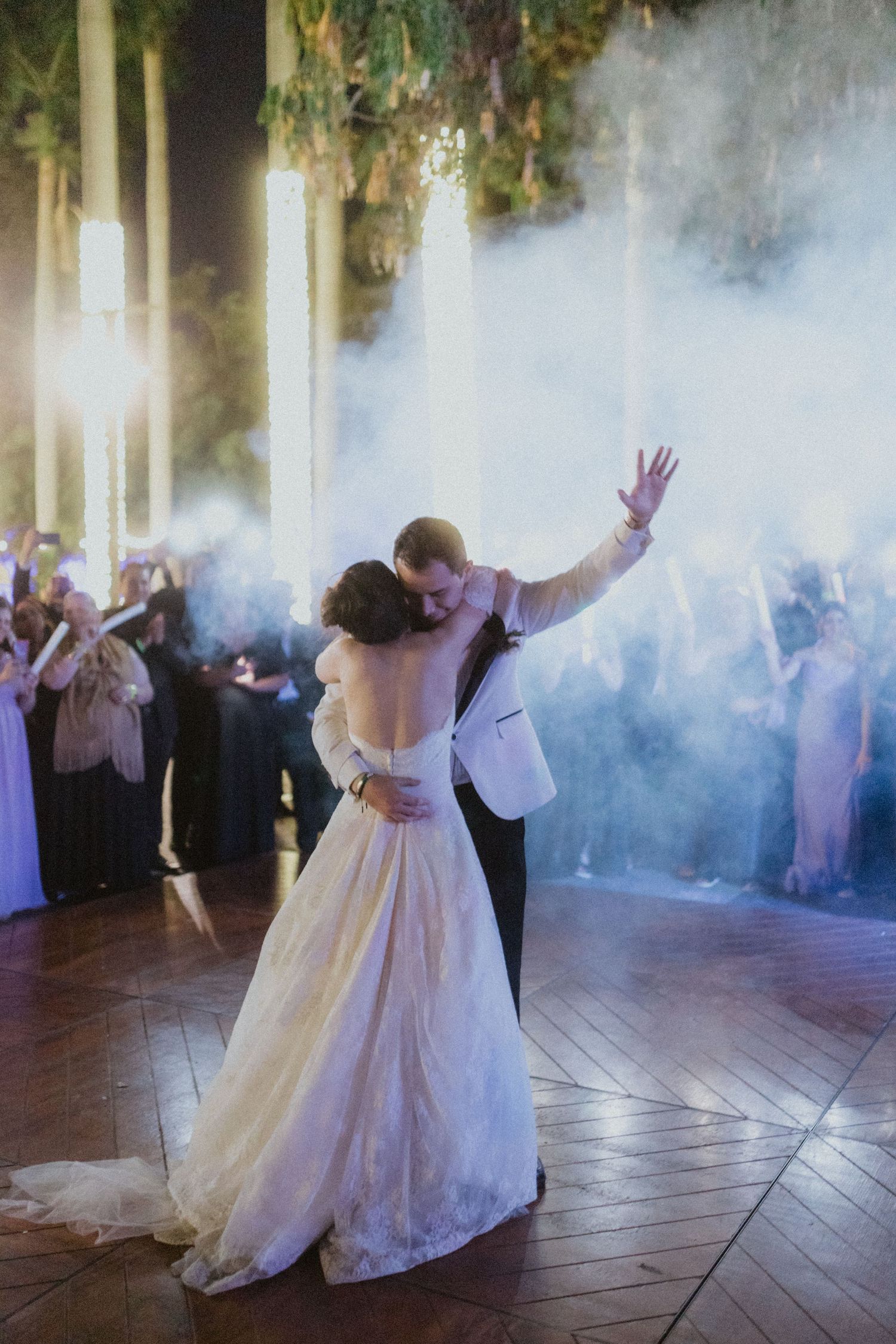 A couple enjoys their first dance at a wedding reception with dramatic fog and lighting effects on the dance floor.