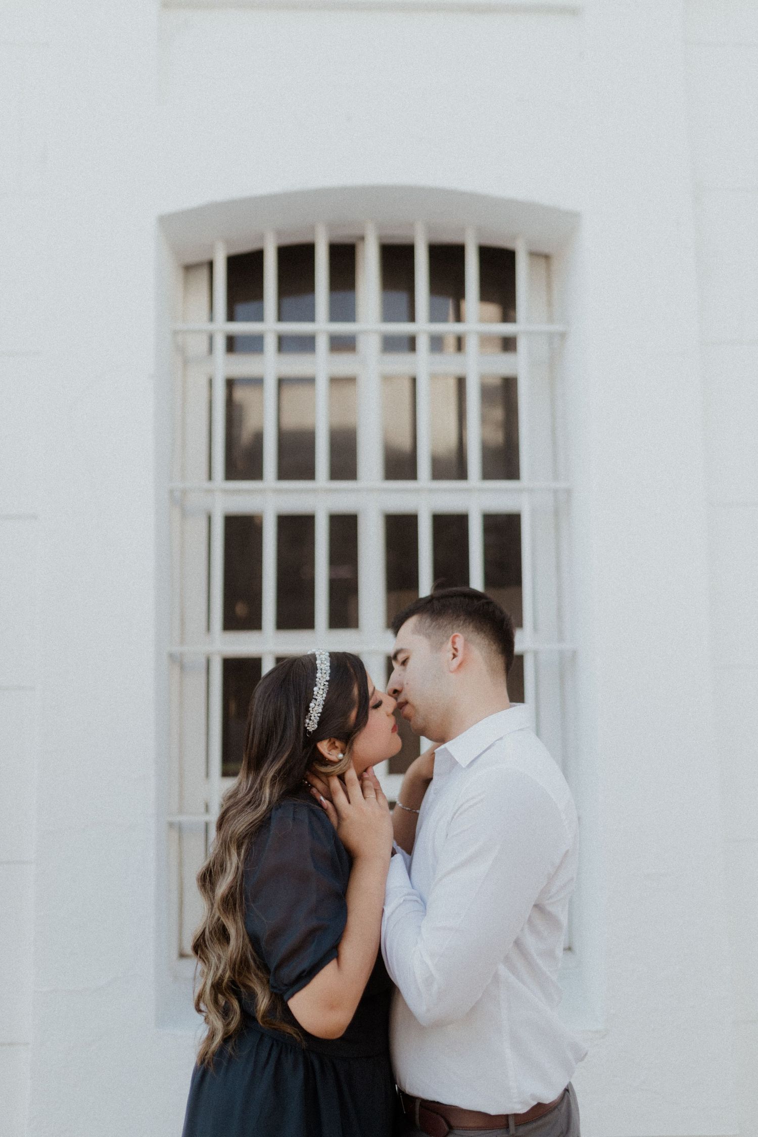 A tender romantic moment captured against a white building with barred windows.