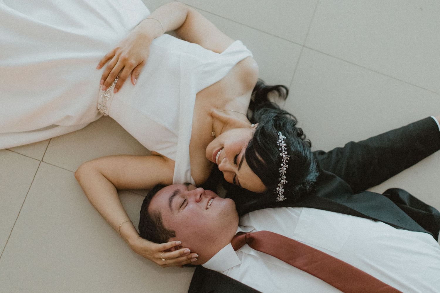 A candid wedding photo showing couple lying on floor in formal attire.