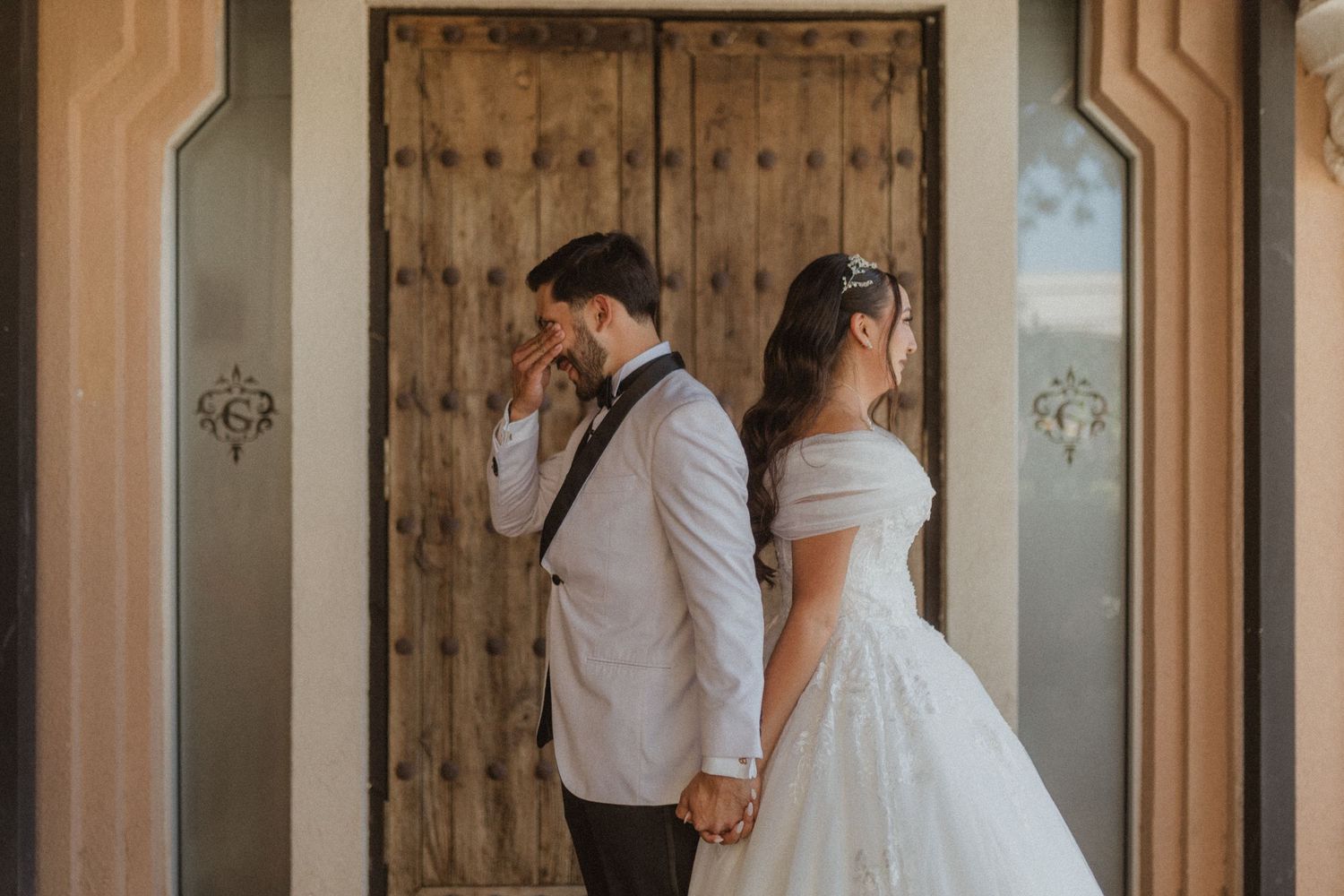 A couple shares an emotional first look moment while standing against a rustic wooden door.