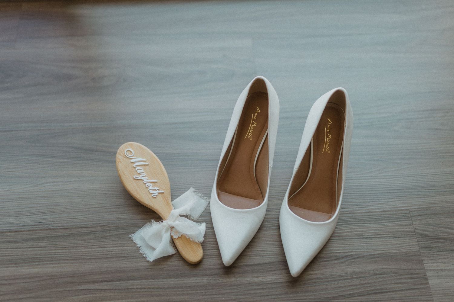 White bridal shoes and accessories arranged on a grey wooden floor.