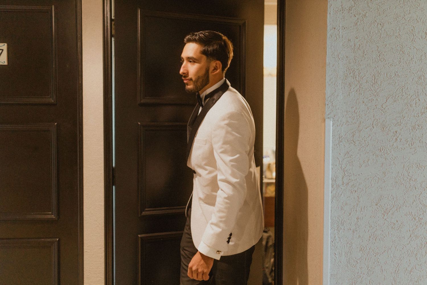 Person in white formal jacket and bowtie standing in doorway.