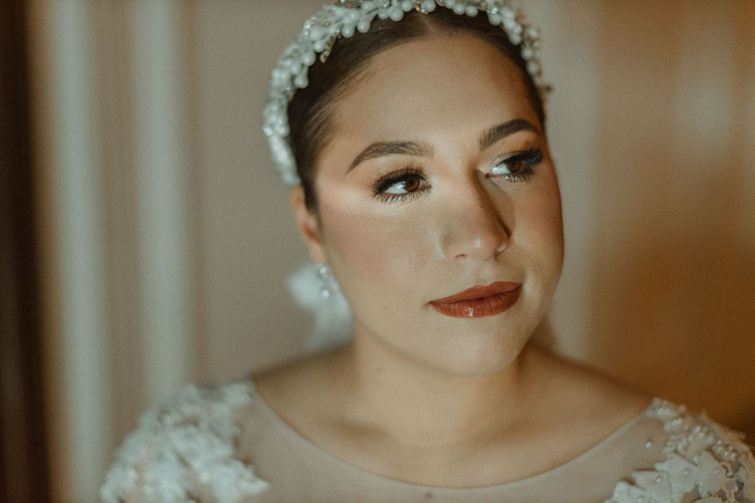 Close-up bridal portrait showcasing elegant makeup and crystal headpiece against warm lighting.