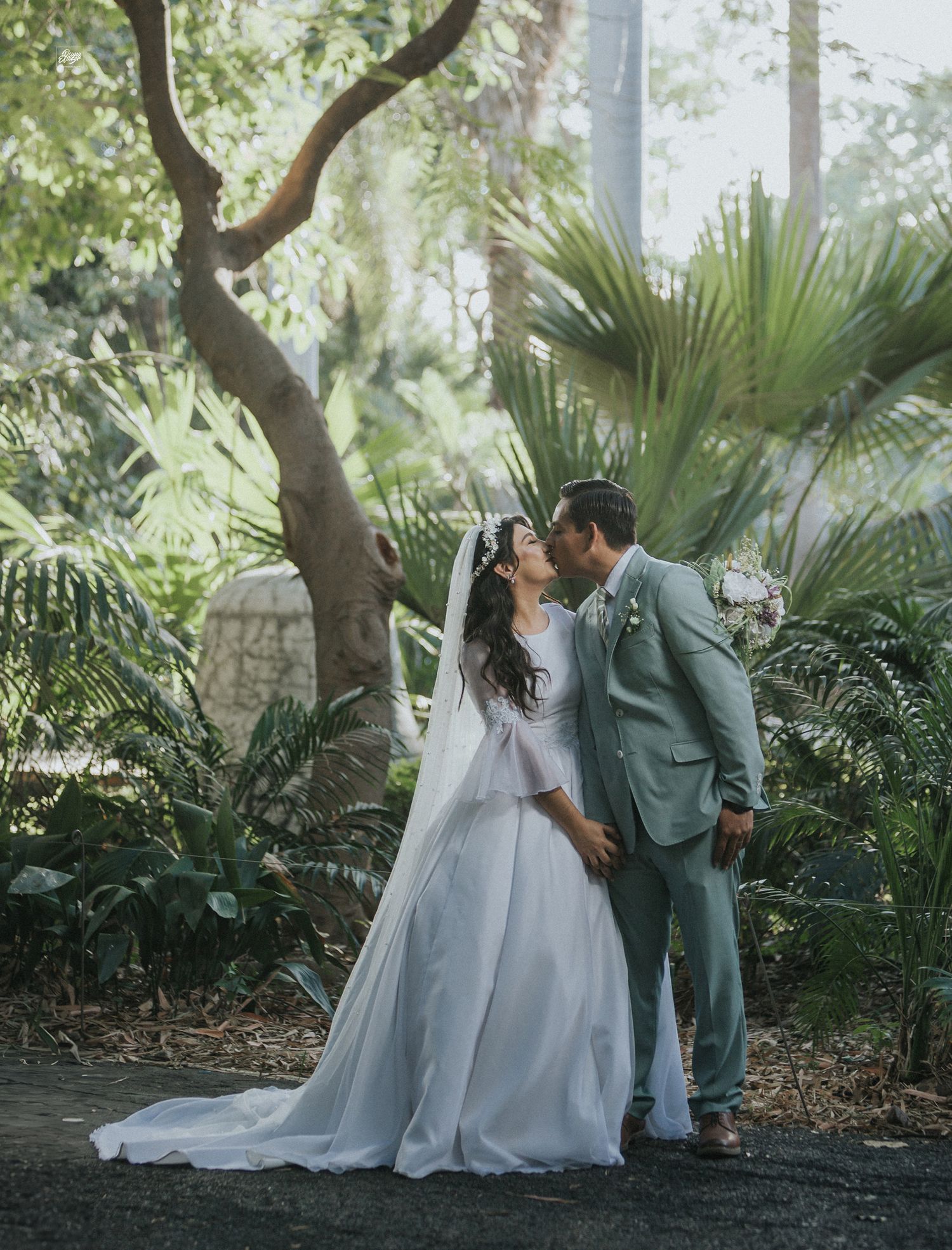 A couple in wedding attire sharing an intimate moment in a tropical garden setting.
