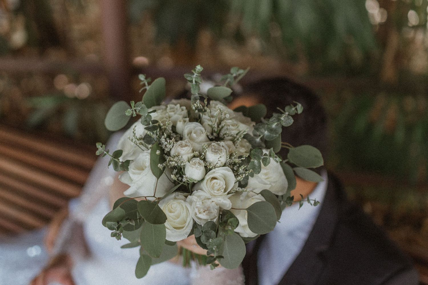 White rose and eucalyptus wedding bouquet held against dark background.