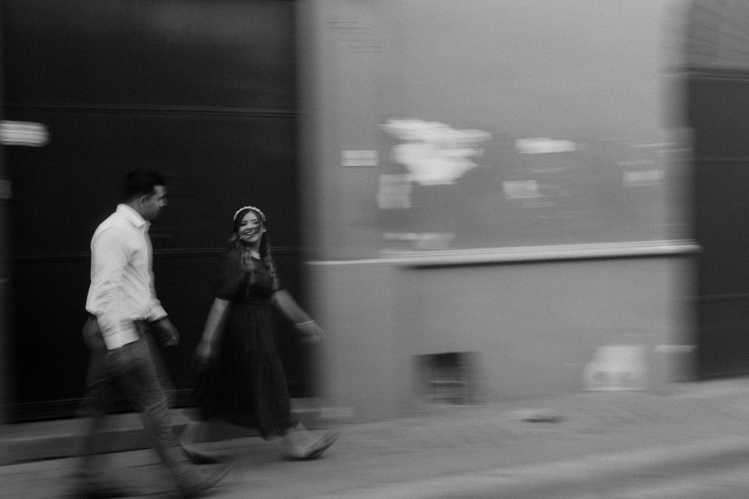 A black and white motion blur photograph of a couple walking together on a city street.