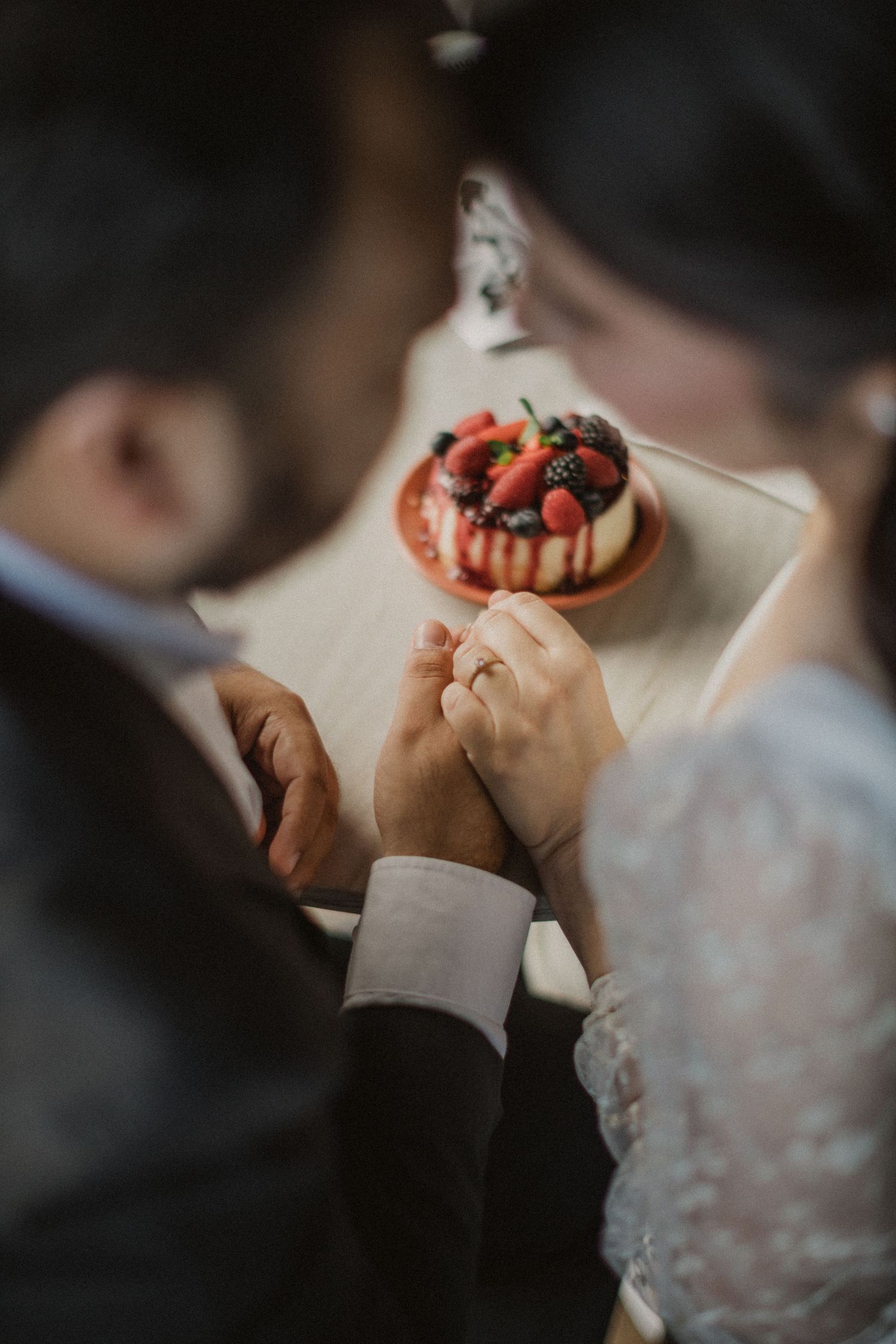 Couple holds hands across table with strawberry dessert in romantic setting.
