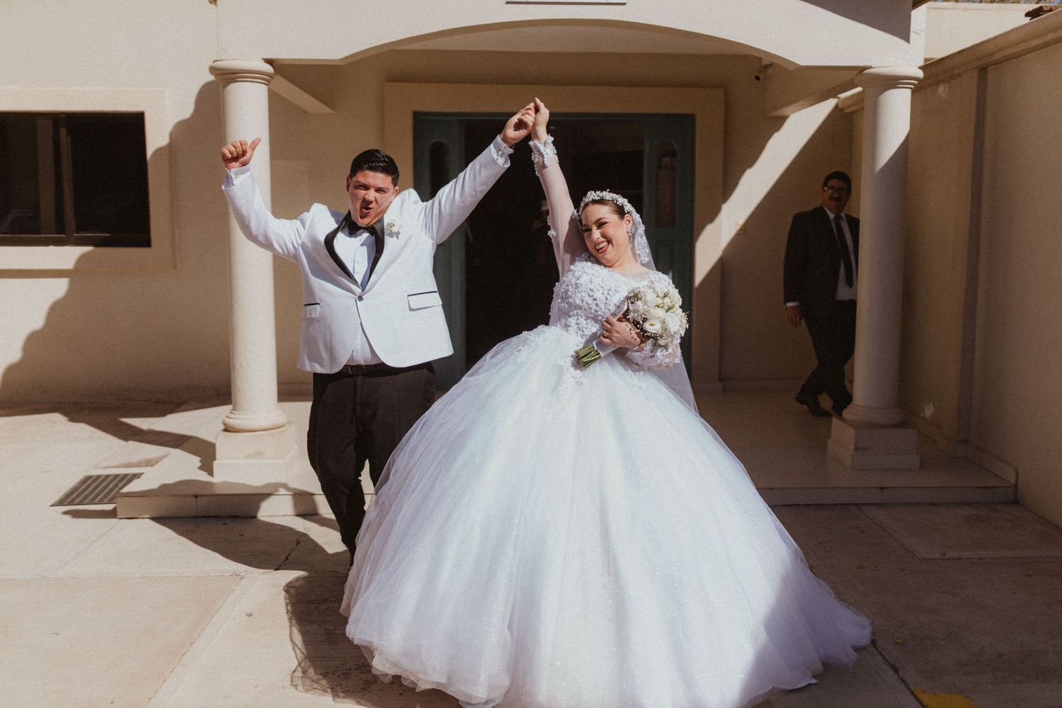 Newlyweds pose and dance in outdoor courtyard with pillars and bright sunlight.