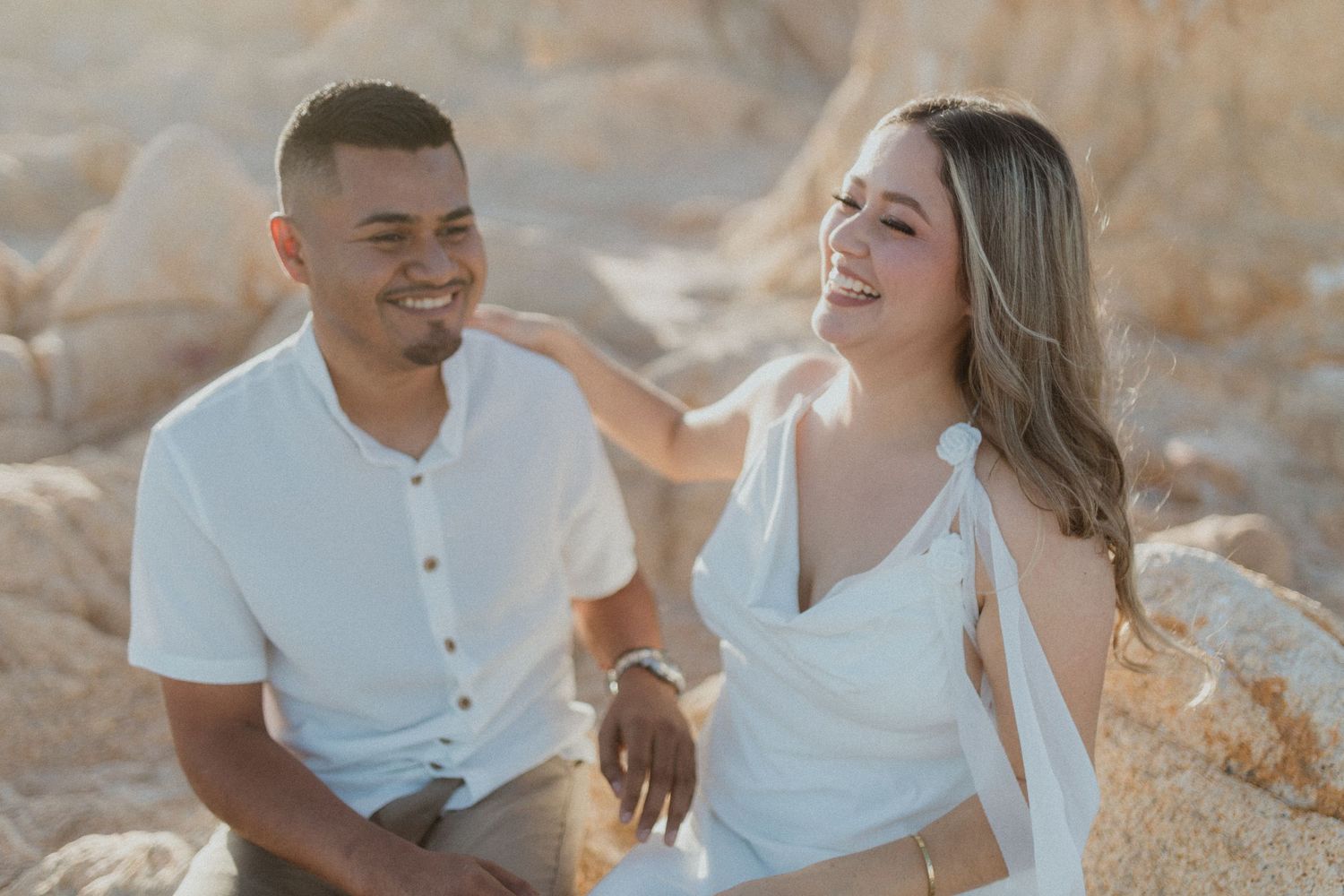 Couple laughing and sharing joyful moments on beach during sunset photoshoot.