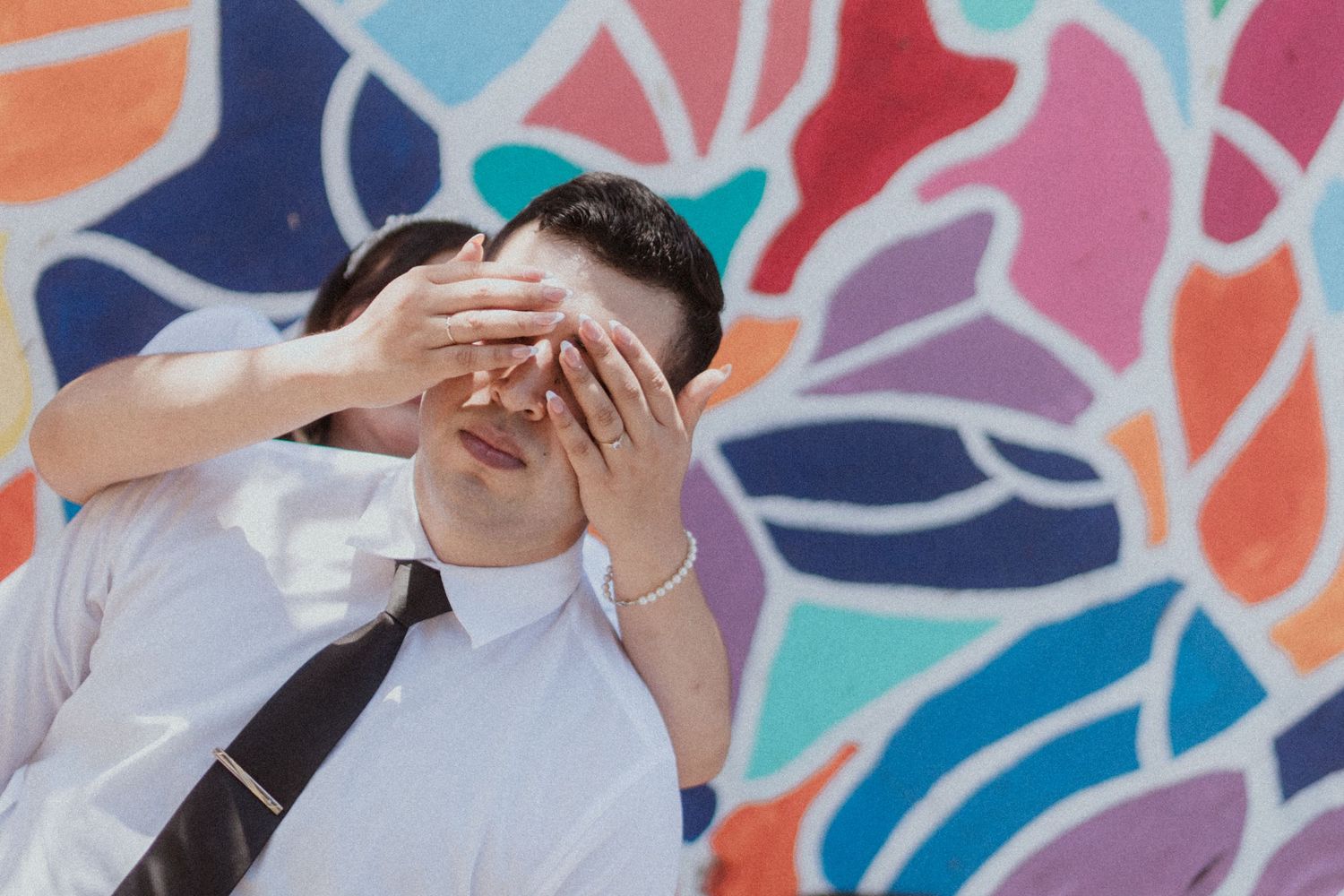 Joyful couple embraces against a vibrant colorful mural wall during a special moment.