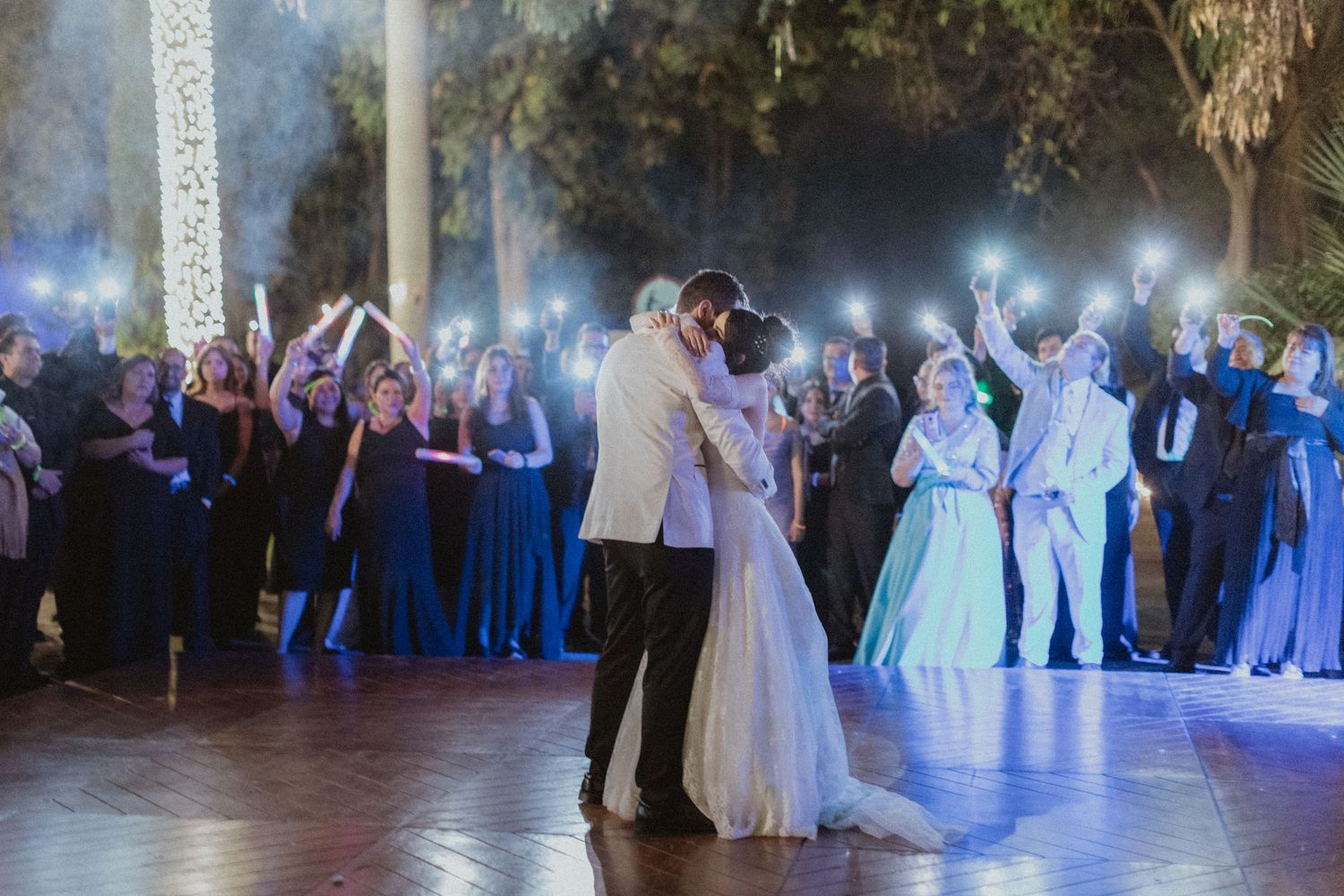 Wedding reception dance floor filled with guests enjoying a celebration under blue lighting.