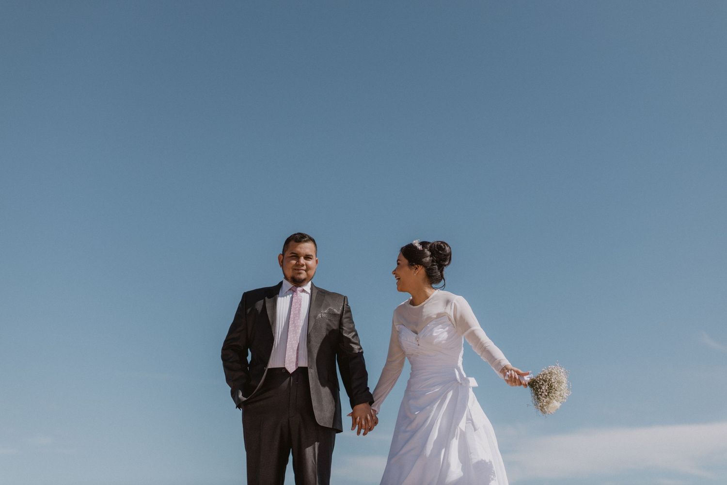 Newlyweds holding hands while walking along seaside cliffs.