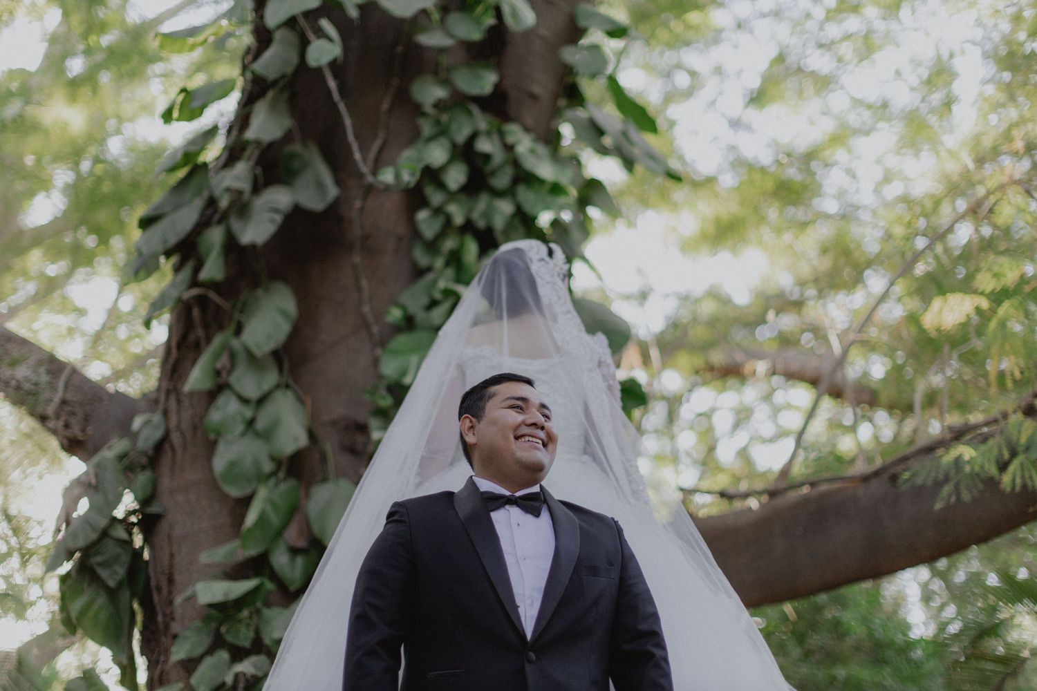 A wedding portrait captured under a sprawling tree with natural lighting.
