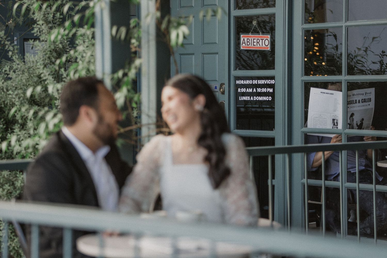 A couple converses outside a storefront with green foliage visible.