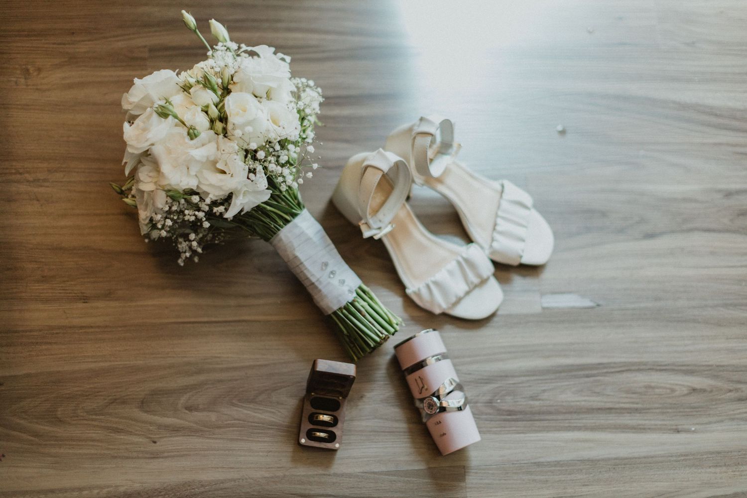 White floral bouquet and bridal accessories arranged on a wooden floor.