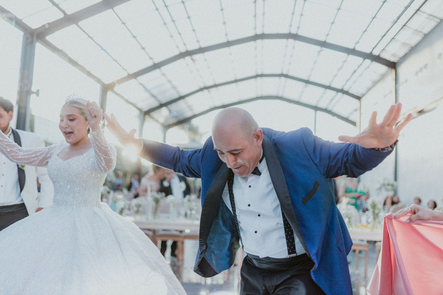 A wedding couple dances together at their reception in a covered outdoor venue surrounded by other dancers.