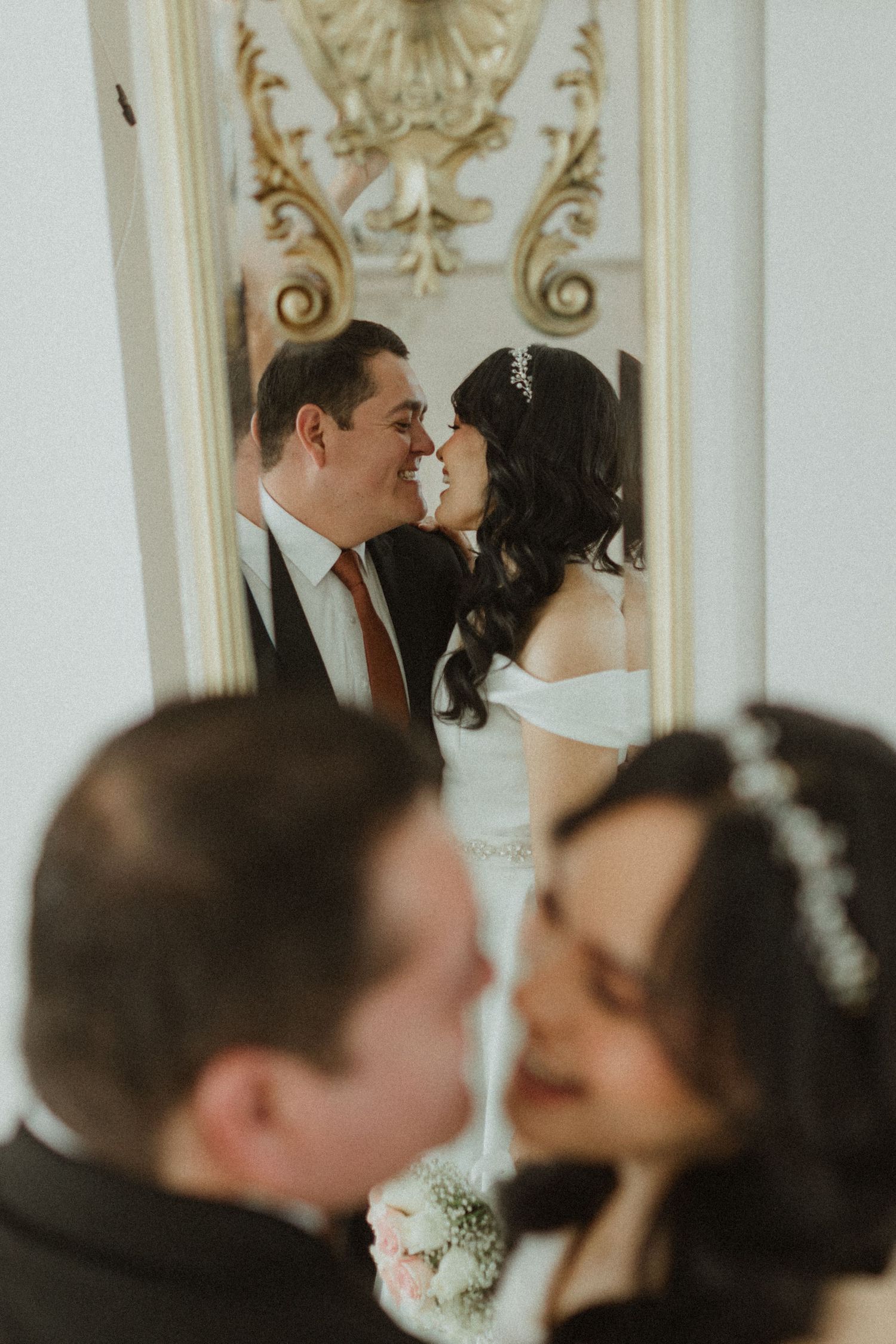 An intimate wedding portrait captured in an ornate mirror reflection with elegant architectural details.