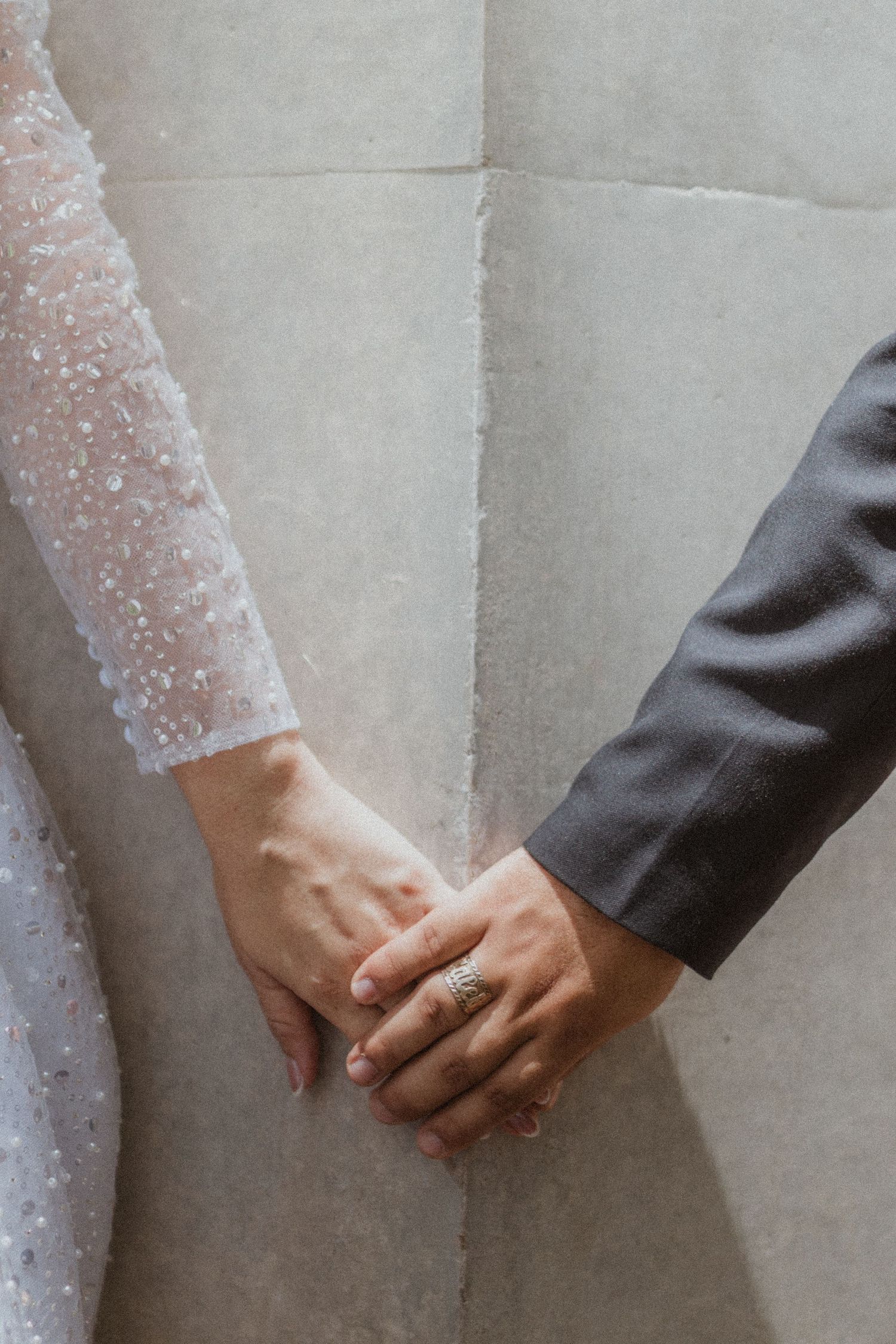 Close-up of bride and groom holding hands, showing delicate lace sleeve details.