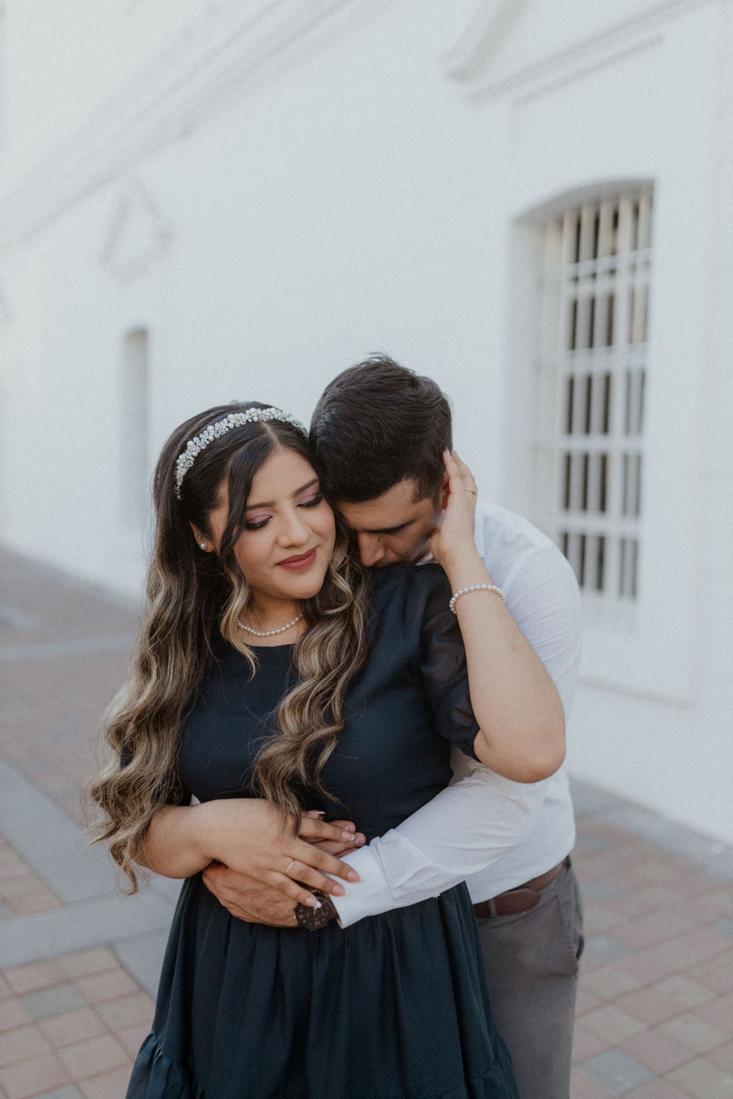 An intimate portrait of a couple embracing against a white wall outdoors.