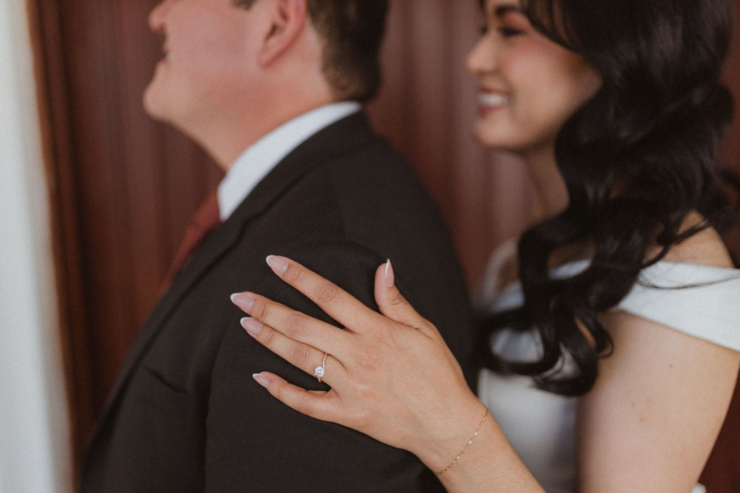 A candid moment shows a bride's hand on her groom's back during their wedding photoshoot.