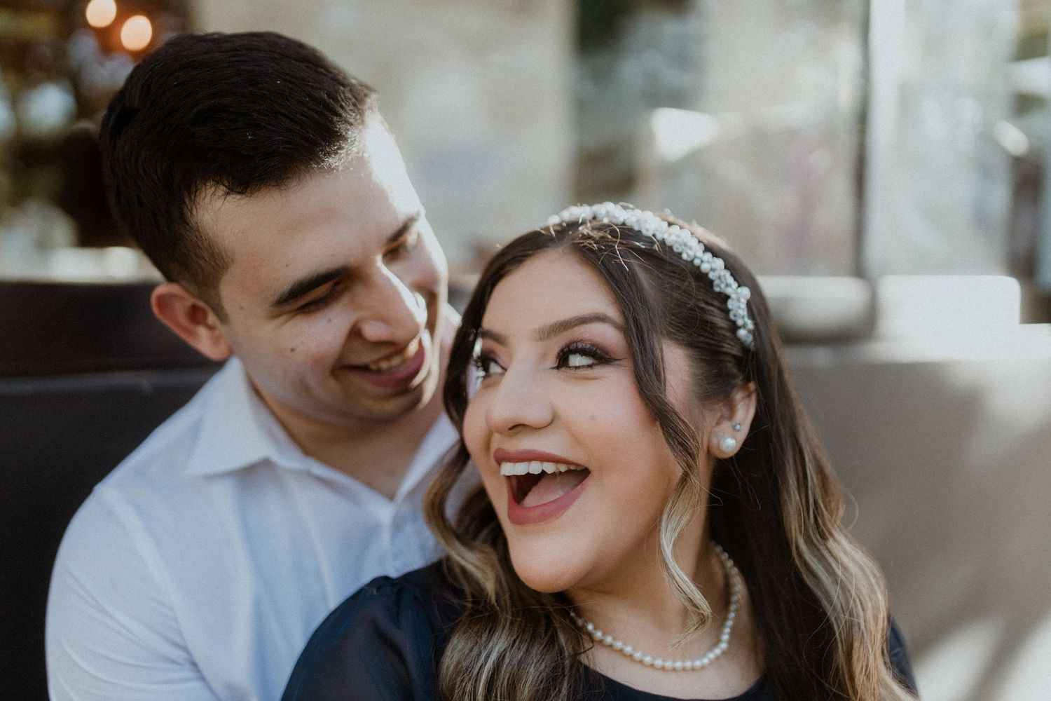 A joyful couple share an intimate moment while wearing white and elegant attire.