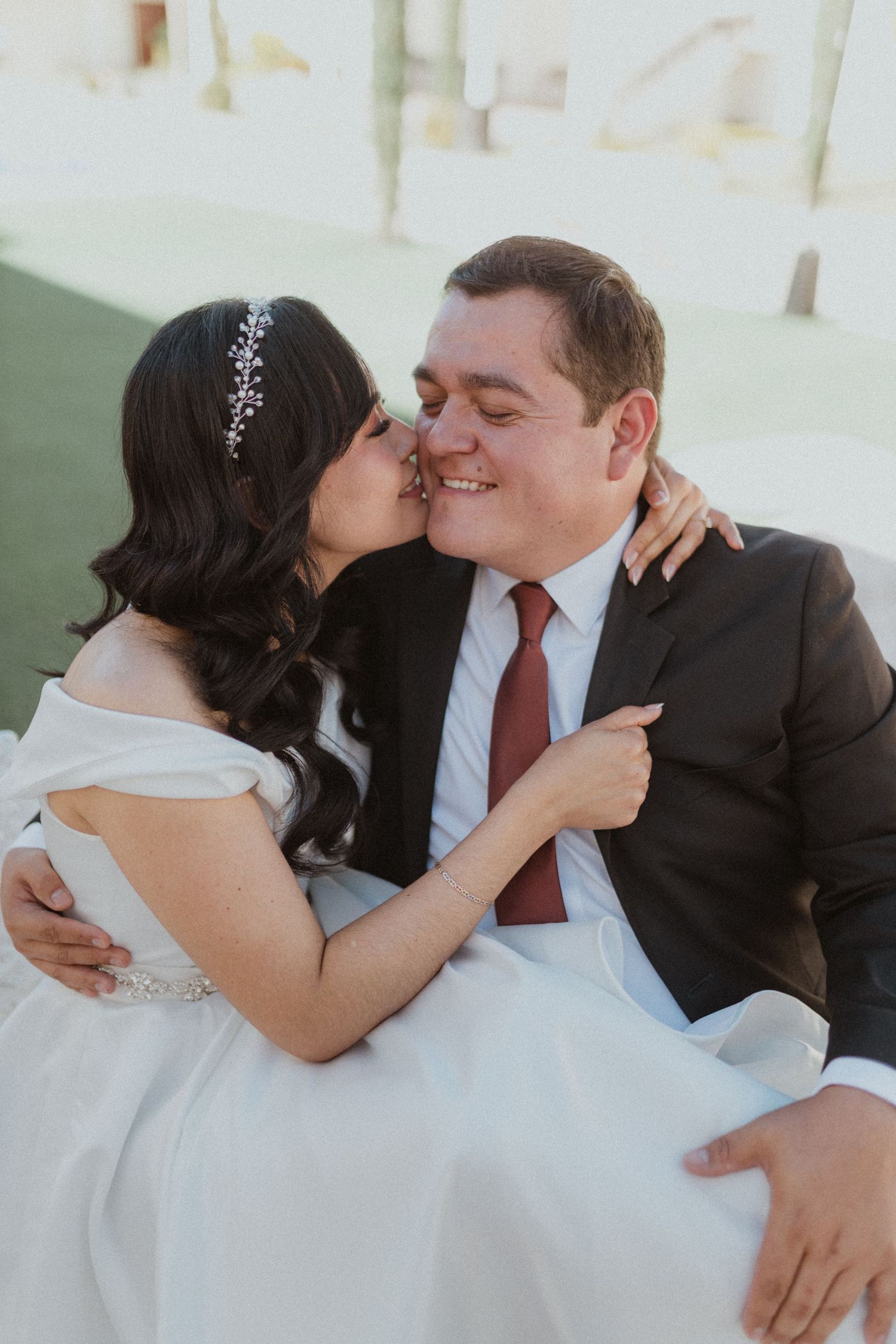 An intimate moment between newlyweds sharing a tender embrace on a white bench.