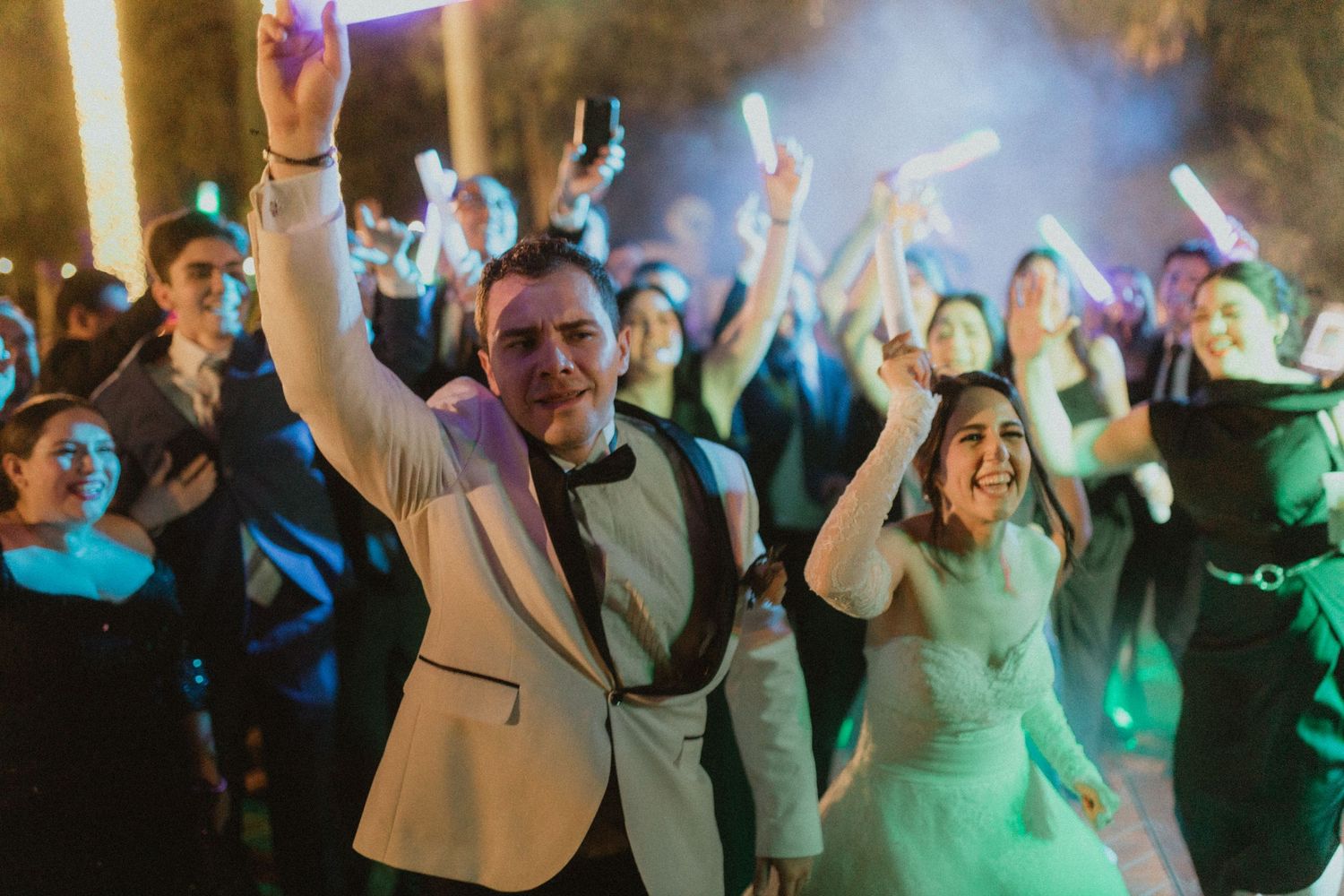 Wedding reception dance party with guests celebrating under colorful lights.