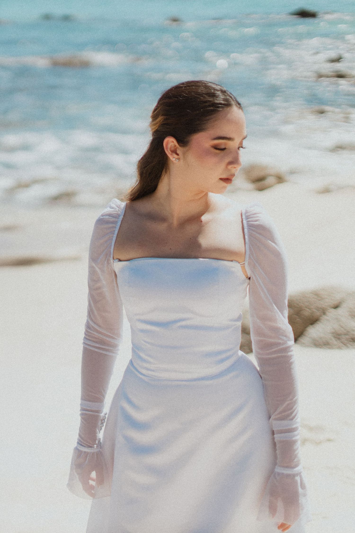 A serene bridal portrait on the beach featuring an elegant white dress with long sleeves.