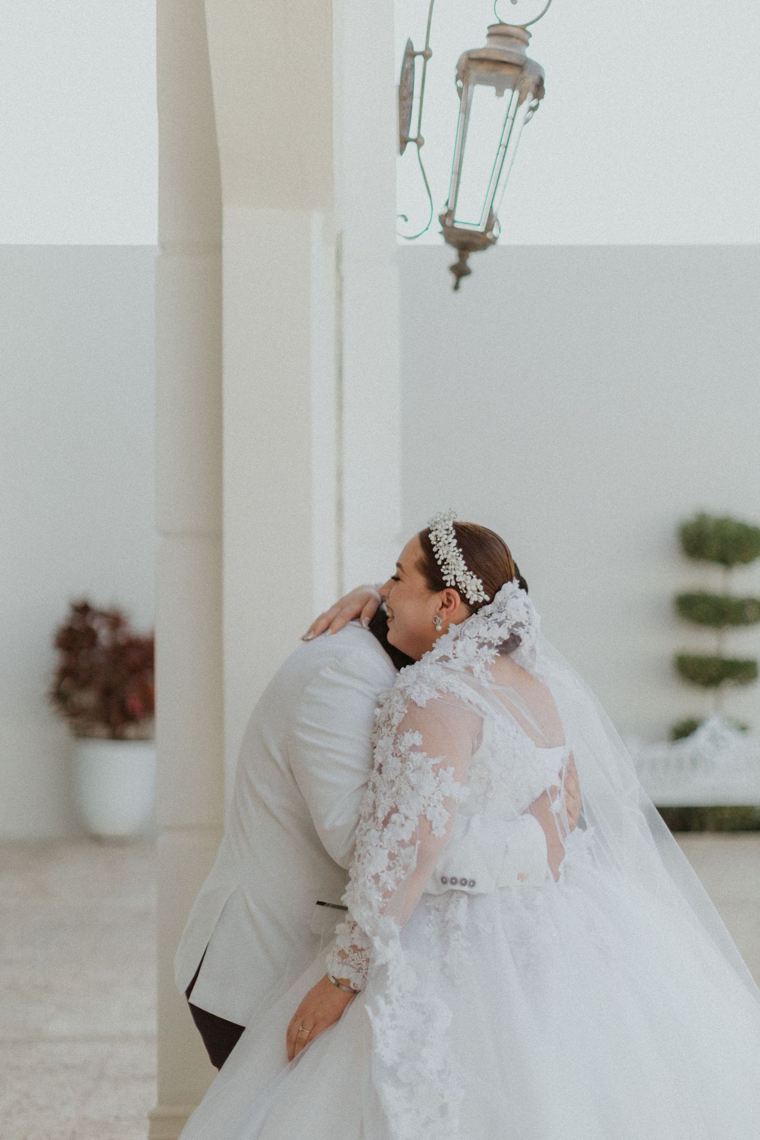 A tender moment between newlyweds embracing under a vintage lantern in a white corridor.