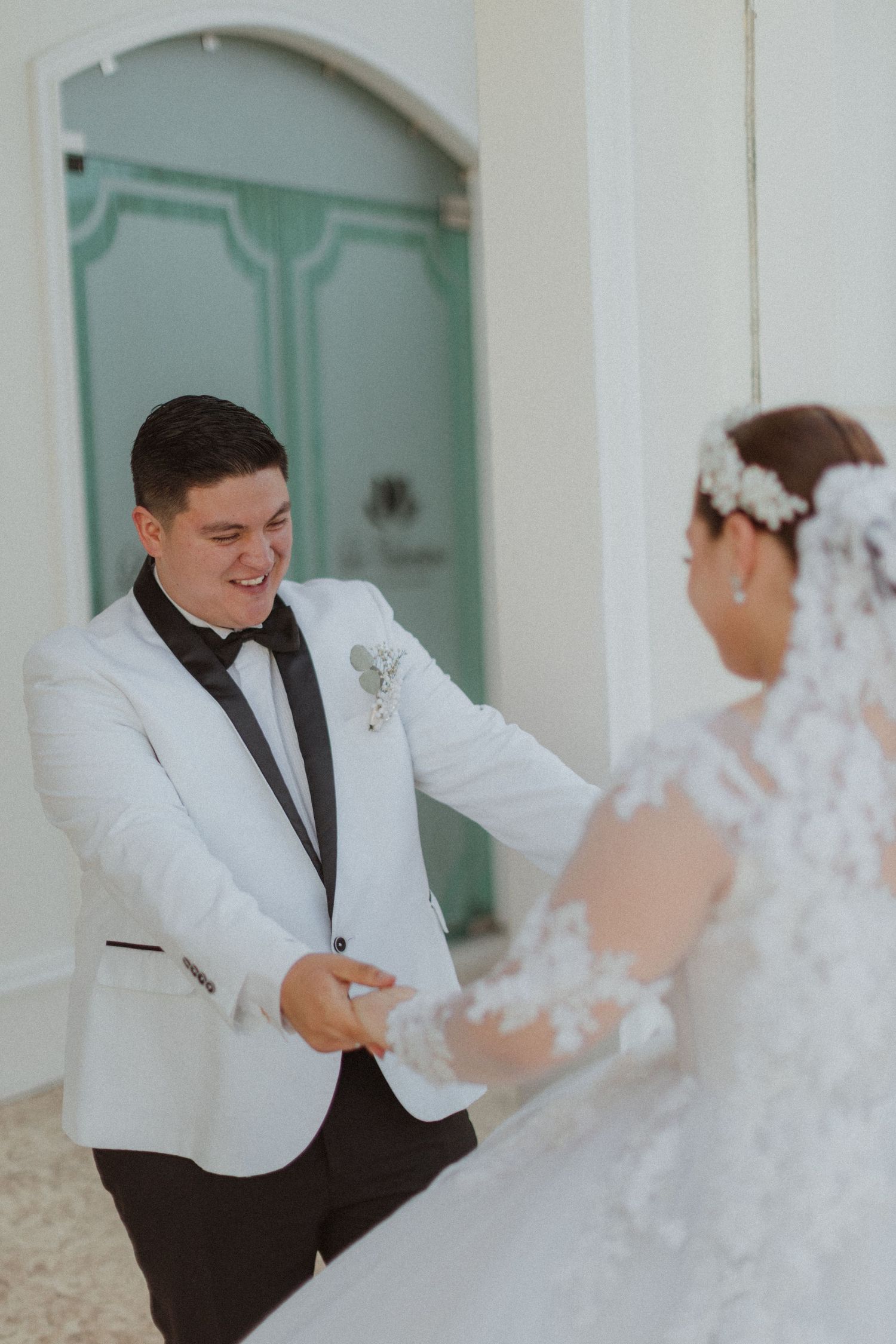A joyful wedding couple dancing and holding hands in an elegant white hallway.