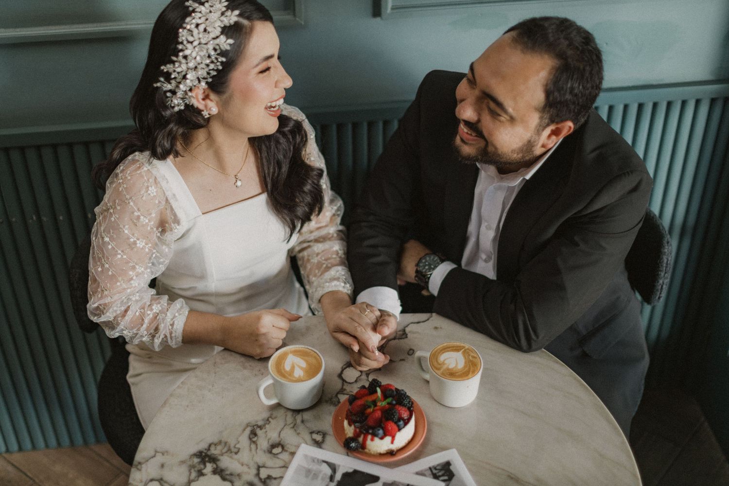 A couple shares coffee and dessert while looking at each other across a cafe table.
