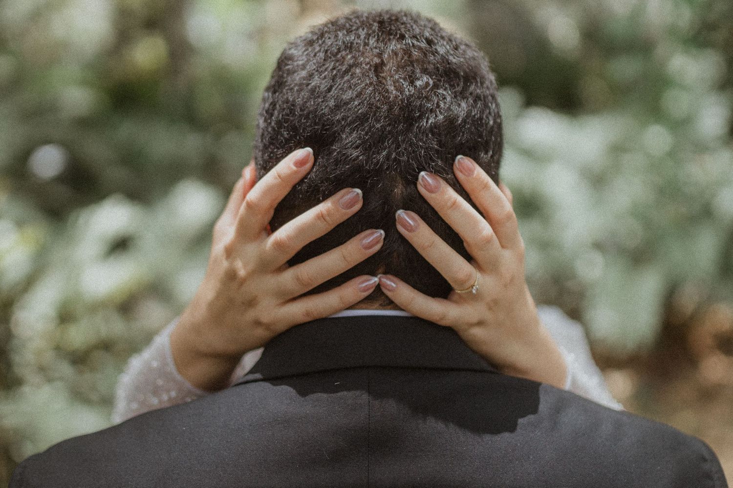 Person wearing black suit jacket touches back of head with both hands.