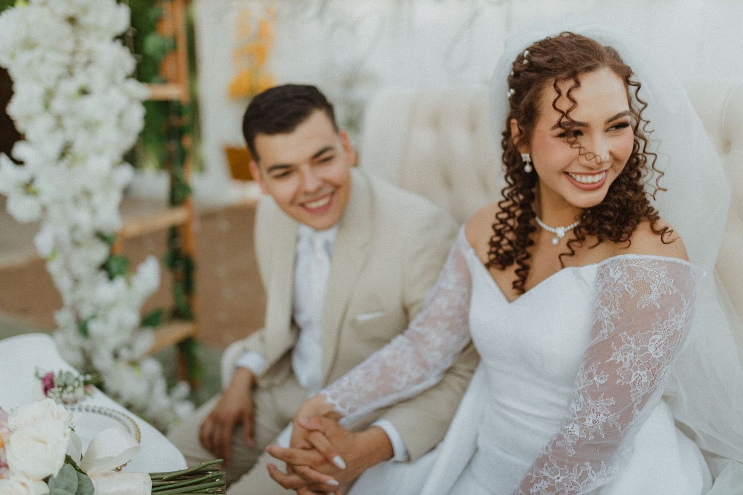 A wedding celebration with a couple seated among white floral decorations.