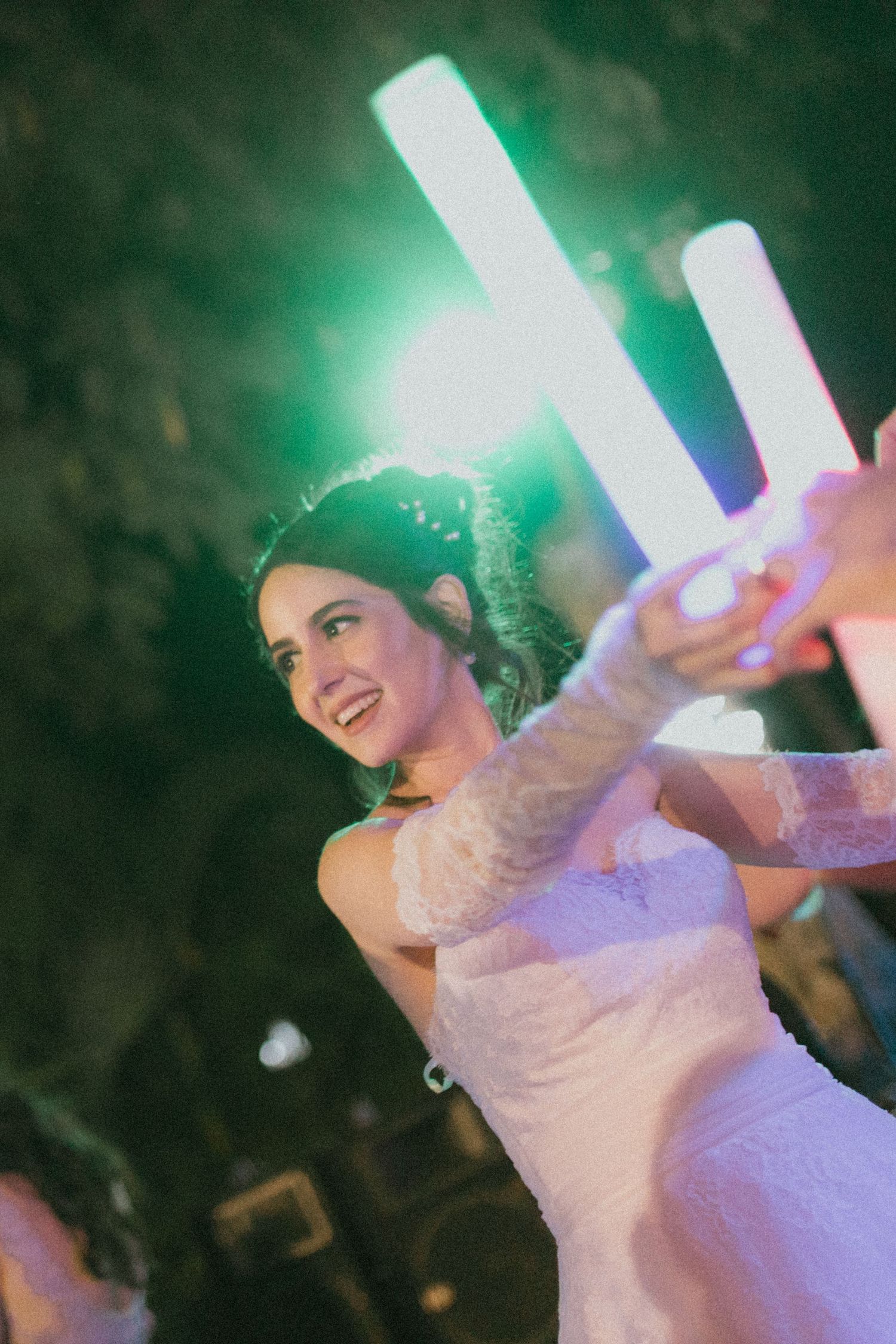 A person in a wedding dress dances with glowing light sticks at a reception.