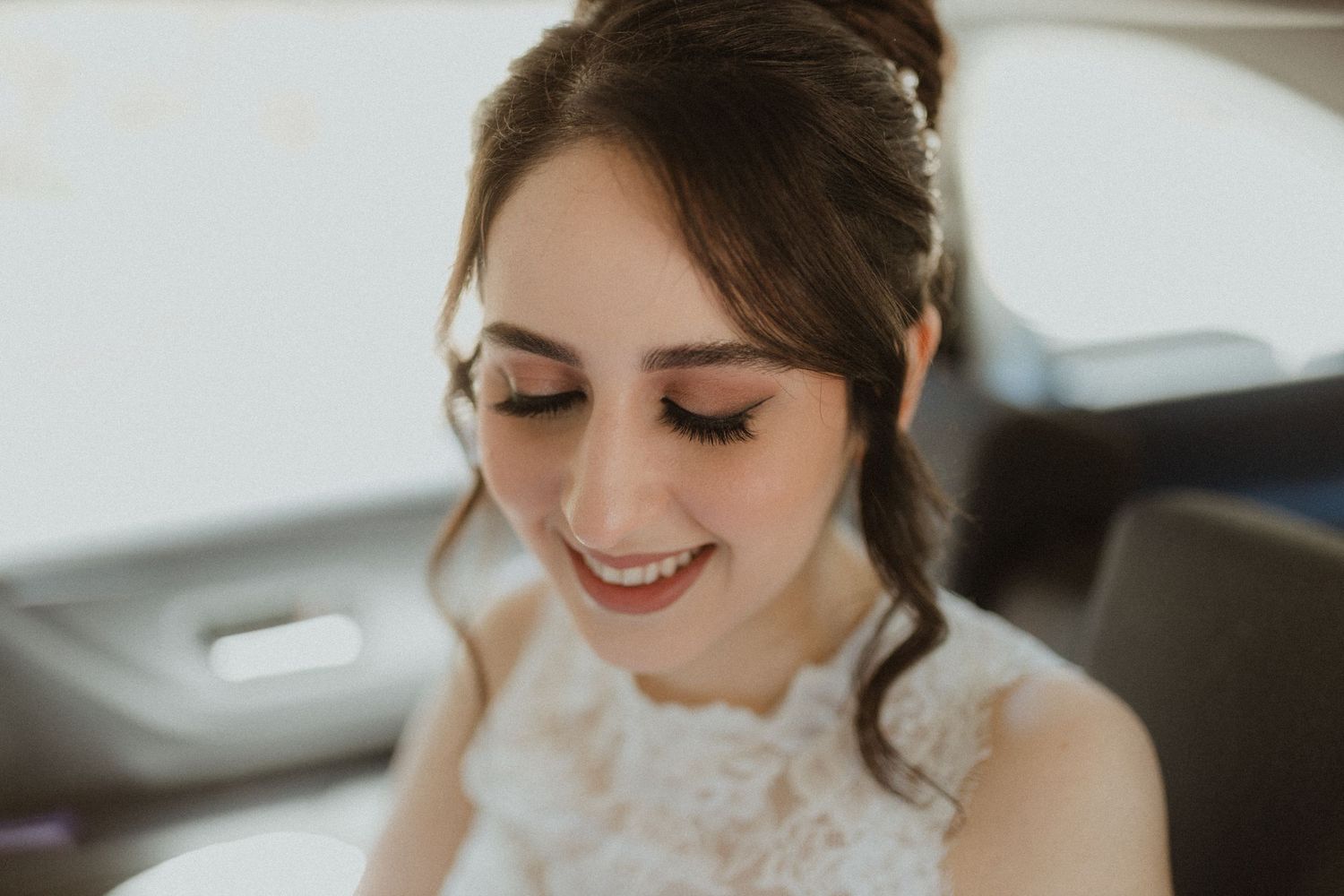 A joyful bride wearing lace dress smiles while sitting in a car.