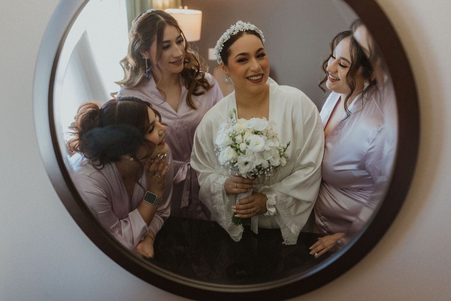 Wedding party preparations reflected in an oval vintage mirror.
