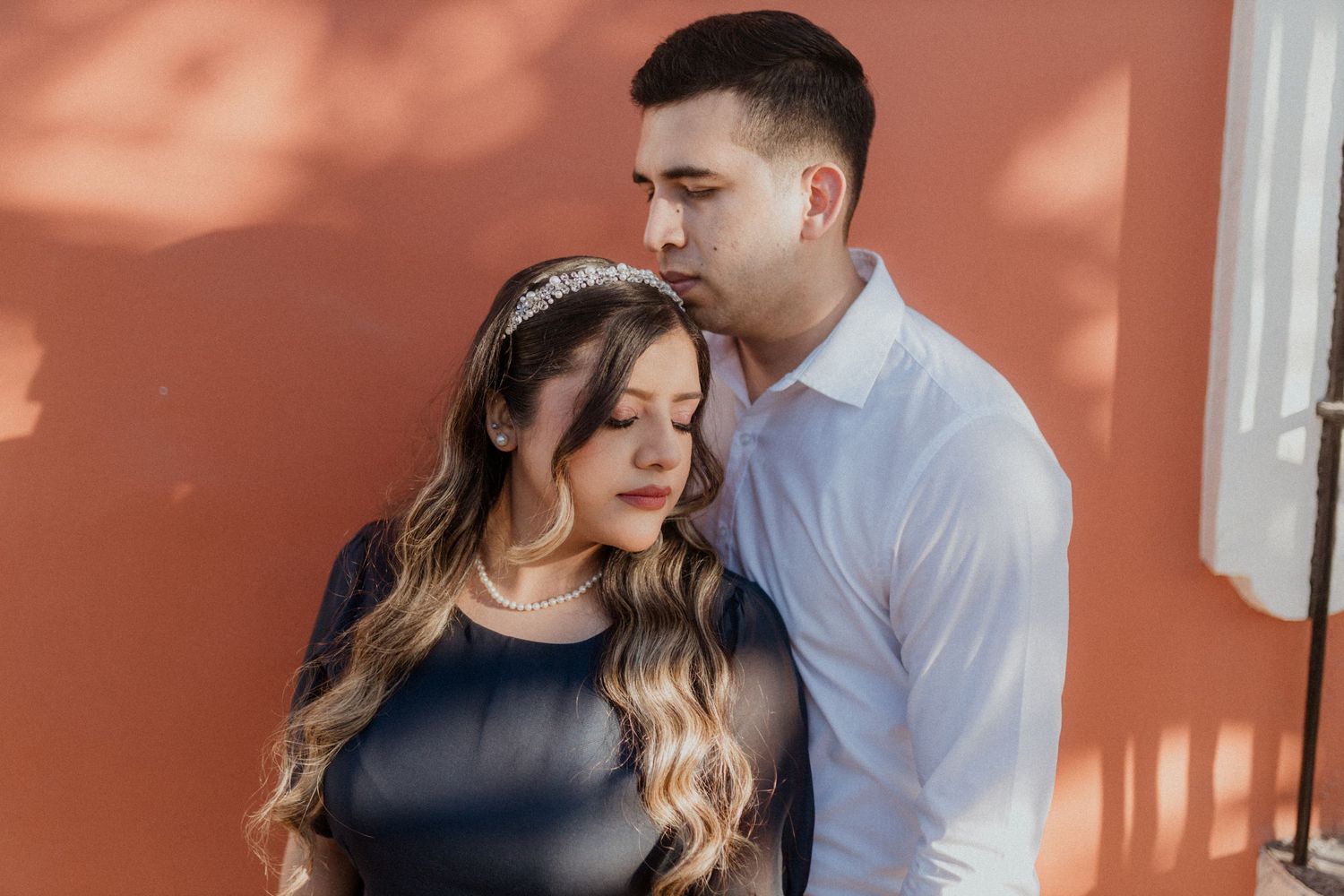 A tender moment between a couple against a sun-dappled terracotta wall.