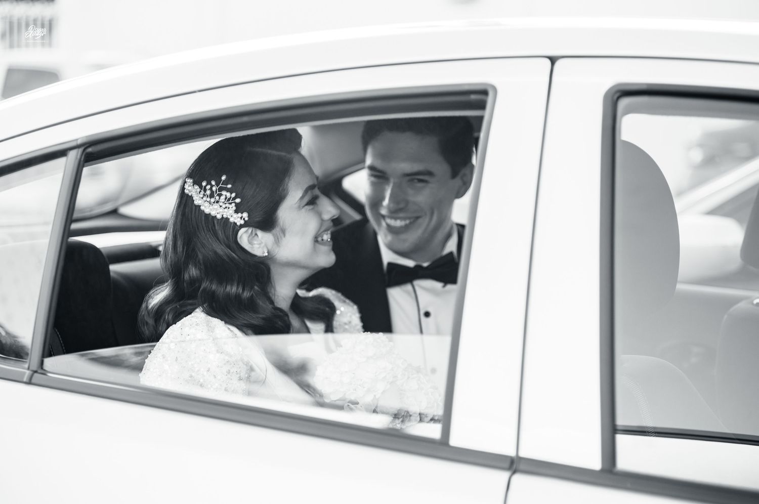 A couple shares a joyful moment inside a car captured in black and white photography.