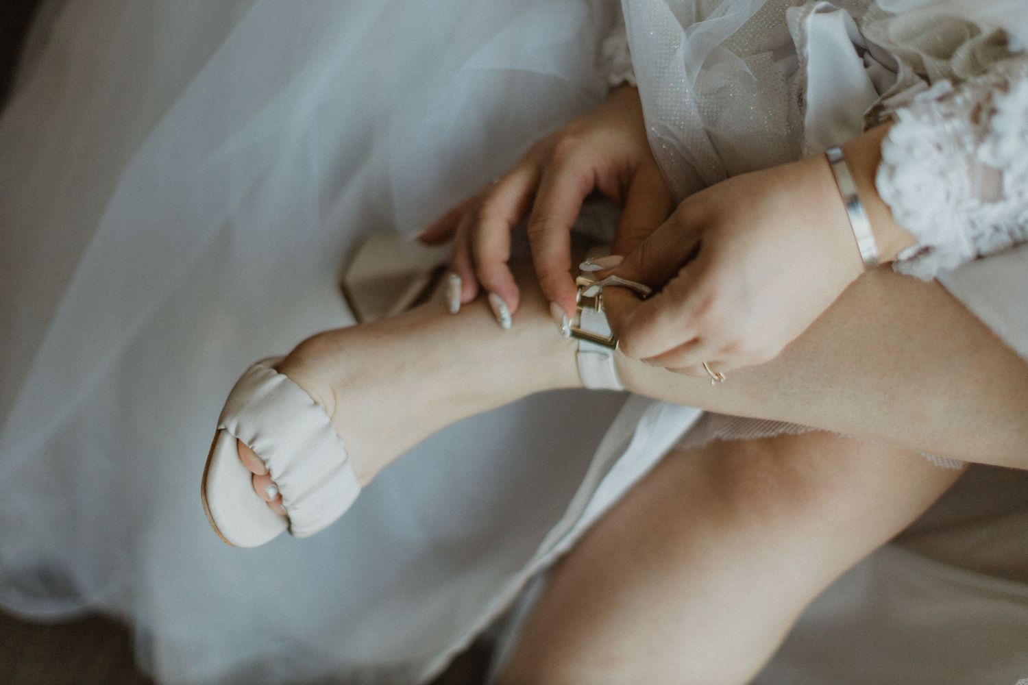 Delicate details of lace and jewelry being adjusted during wedding preparations.