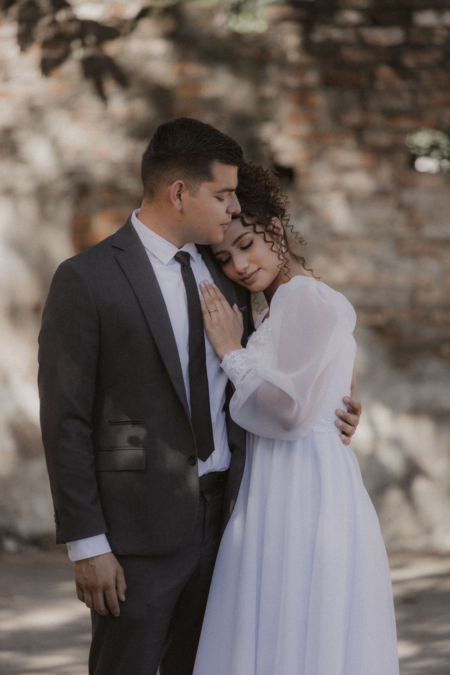 An intimate wedding portrait against a rustic stone wall backdrop.