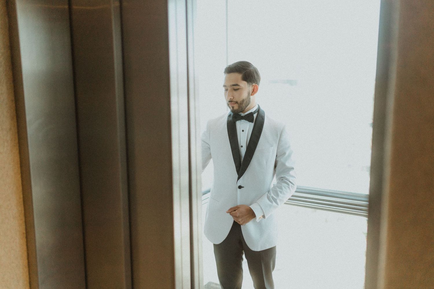 A person in a white suit jacket sits in an elegant bar area with pendant lighting and wooden floors.