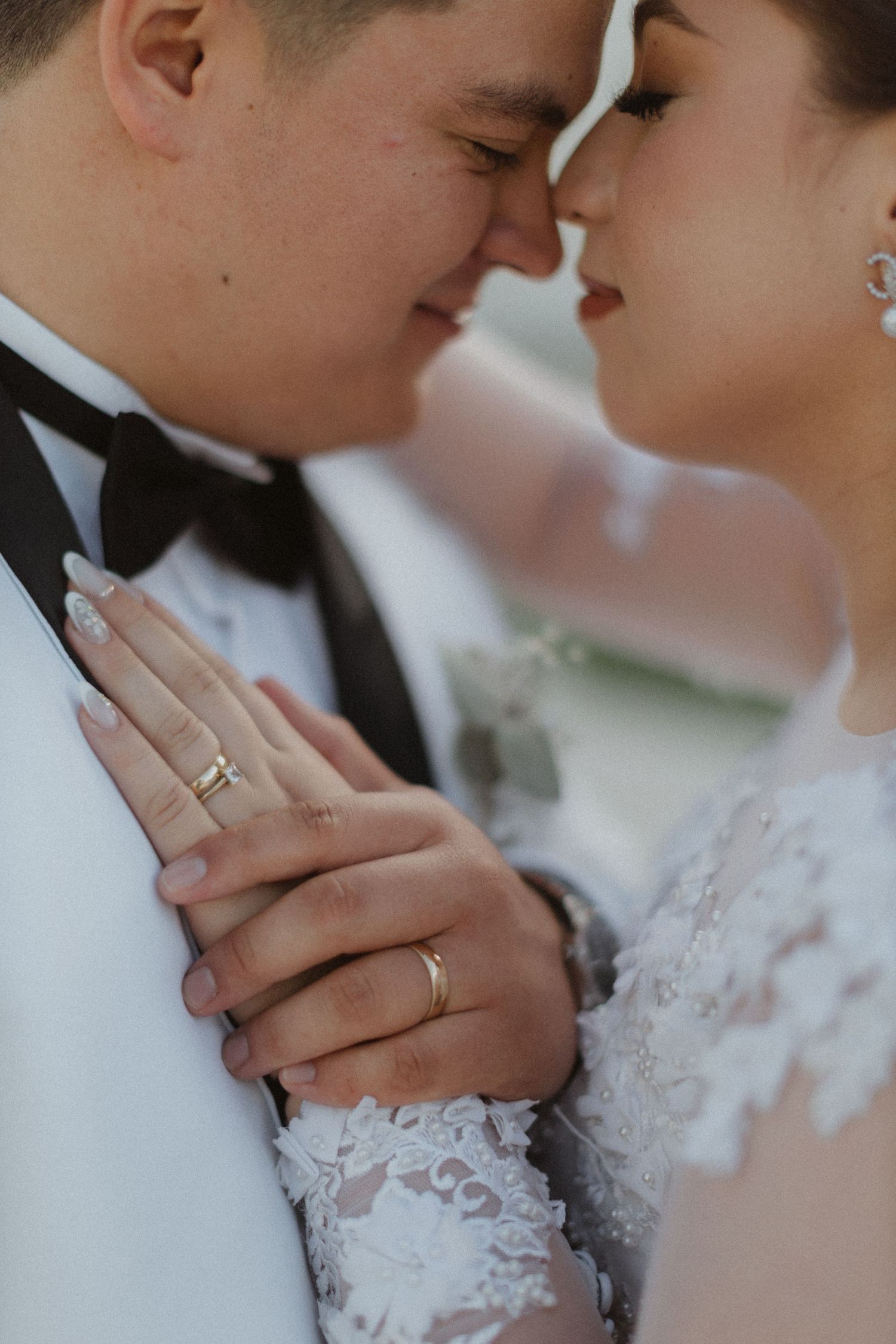 Close-up of couple's hands with wedding rings against white formal attire and lace details.