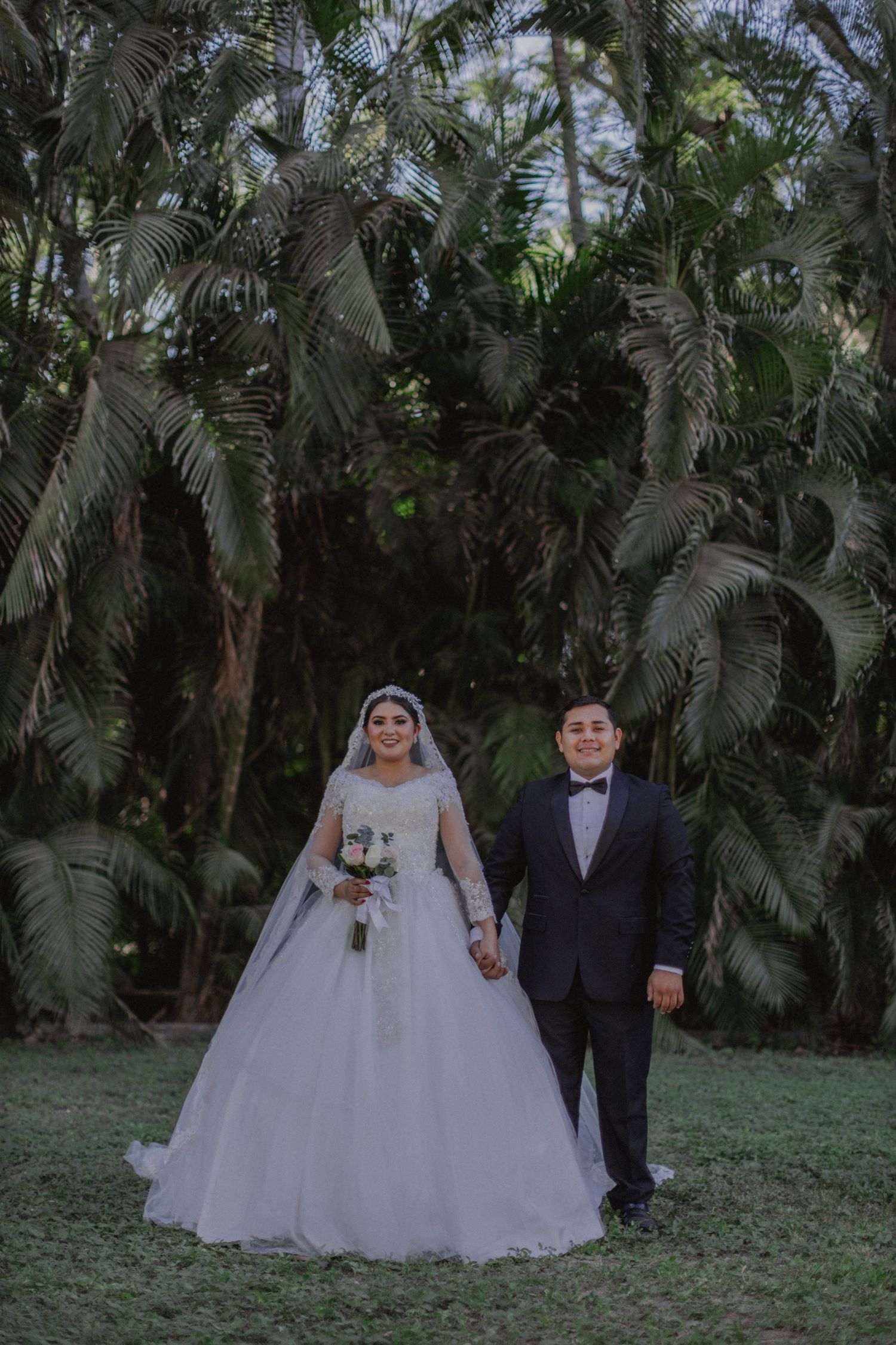 A wedding couple poses in a tropical garden setting with palm trees.