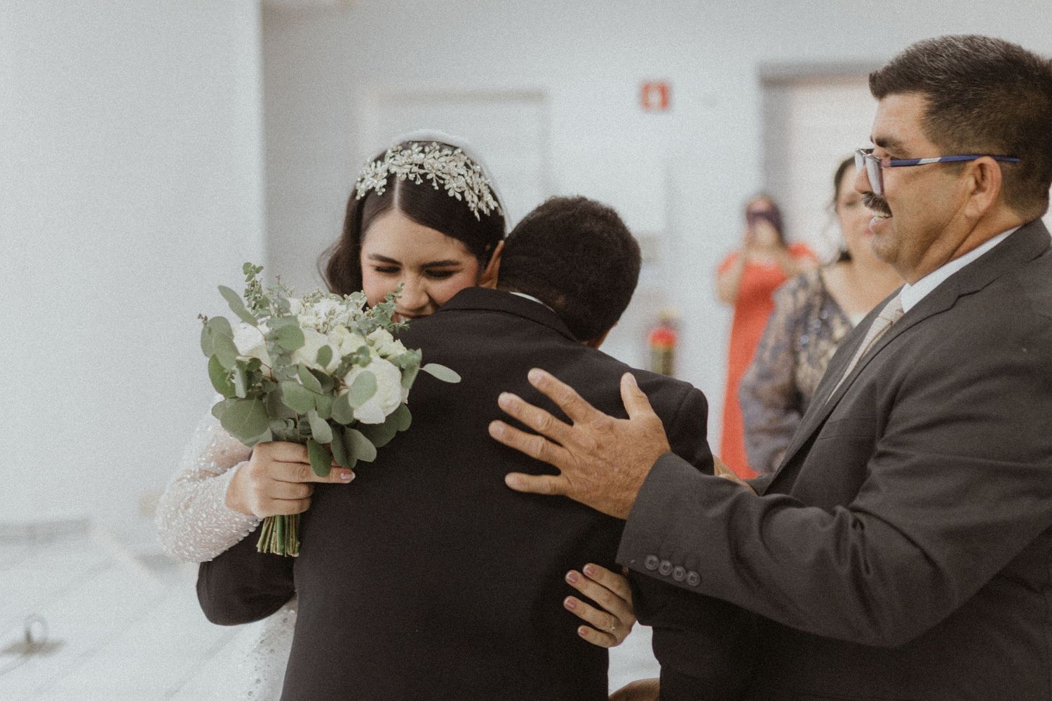 Wedding guests and family share embraces during an indoor ceremony celebration.