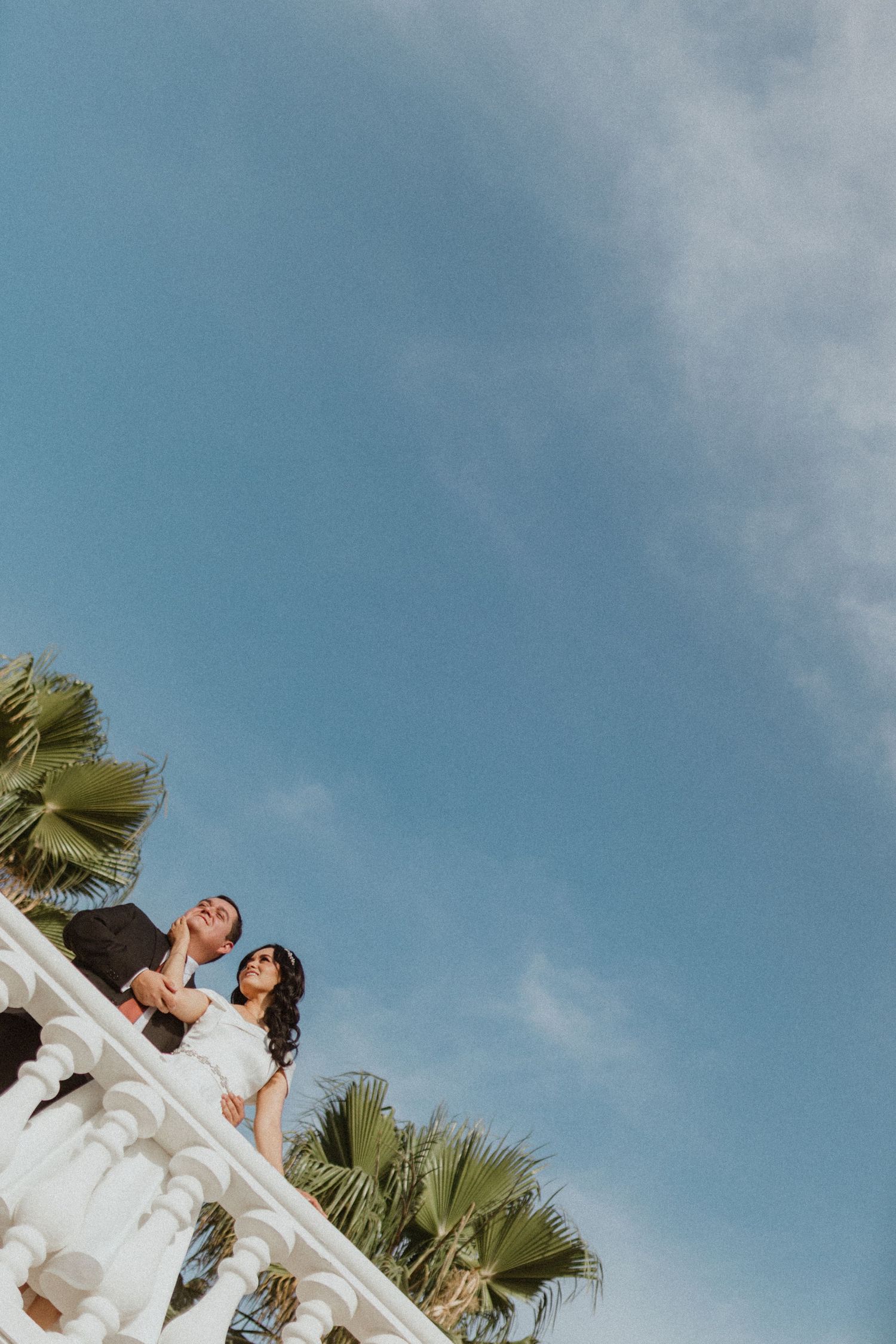 White wedding couple portrait against blue sky and palm trees.