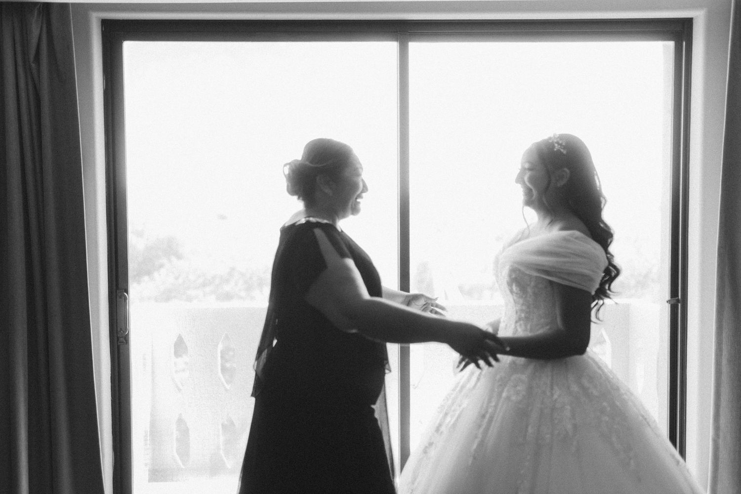 Silhouetted figures stand near large windows during an intimate wedding moment.