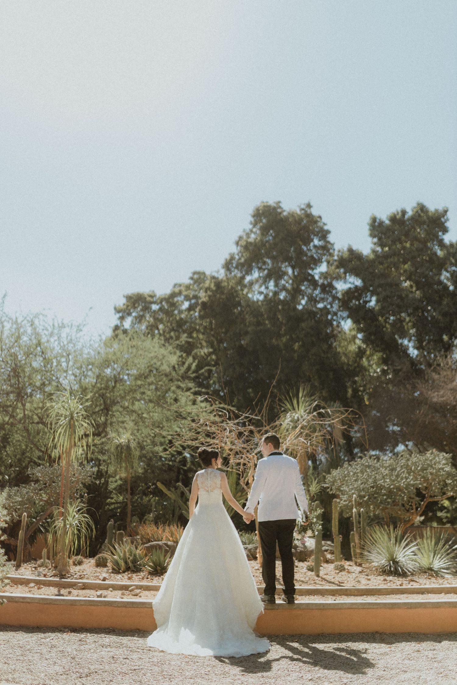 Newlyweds walk together on garden path surrounded by desert landscaping.